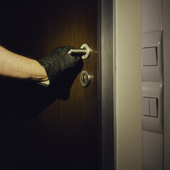 Man hand in a black glove opens the office door in the night light of a flashlight