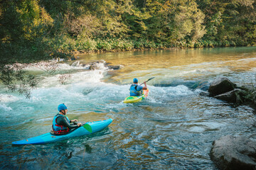 Two whitewater kayakers paddling on the waters of river. Adrenaline seekers and nature lovers. - obrazy, fototapety, plakaty