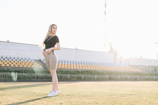 Photo of Athletic Girl in Stadium at Wide Angle from Bottom. Healthy Woman Looks Away in Sunbeams.