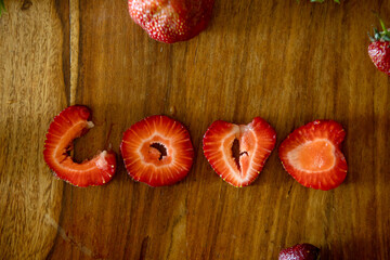 Love sign made from strawberry pieces on a table, whote strawberries around