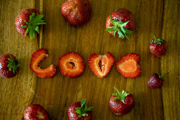 Love sign made from strawberry pieces on a table, whote strawberries around