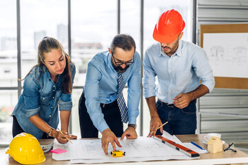 Professional of team architect industrial engineer cargo foreman in helmet working new construction project architectural plan with blueprint and construction tool at the building construction site