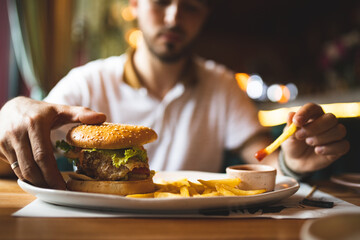 Man eating a burger. Close-up of a burger on the table. Fast food. Man eating a cheeseburger. Unhealthy food.