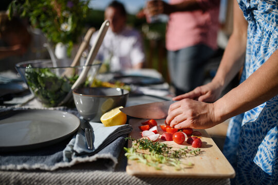 Unrecognizable woman cutting vegetables on wooden board during weekend barbecue in yard, outdoor, prepare for grilling,