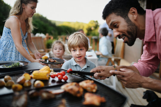Father grilling meat and vegetable on grill during family summer garden party.