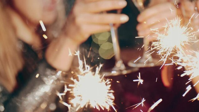 Close up portrait of friends at party celebrating birthday, drinking champagne or sparkling wine, pouring into glass, smiling, laughing, holding and waving sparkler. Happiness or fun concept.