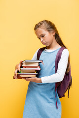 Upset preteen schoolgirl looking at books isolated on yellow.