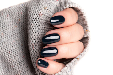 Female hand in gray knitted sweater with beautiful manicure - dark black nails. Nail care concept