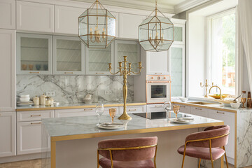 a close view of the white stylish kitchen with a cooking island in the luxurious interior of a modern apartment in light colors with stylish furniture.