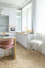 a close view of the white stylish kitchen with a cooking island in the luxurious interior of a modern apartment in light colors with stylish furniture.