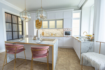 a close view of the white stylish kitchen with a cooking island in the luxurious interior of a modern apartment in light colors with stylish furniture.