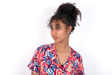 Young African American woman wearing colourful dress over white wall, looks pensively aside, plans actions after university, imagines what to do Thinks over about new project.