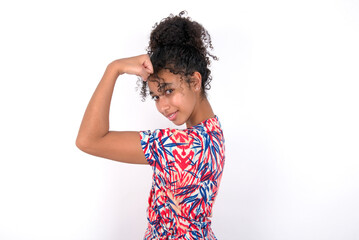 Fototapeta na wymiar Young African American woman wearing colourful dress over white wall, showing muscles after workout. Health and strength concept.