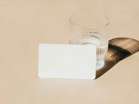 White blank card for text mockup and glass of water on beige background.