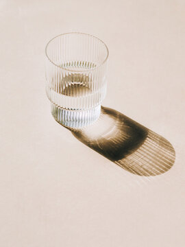 Glass of water and long shadow from sunlight on beige background