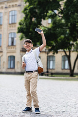 Positive asian schoolkid holding laptop and smartphone outdoors.