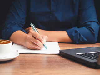 Hand holding a pen writing on a paper over a wooden desk while sitting in the office