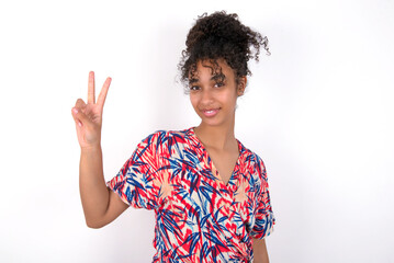 Young African American woman wearing colourful dress over white wall showing and pointing up with fingers number two while smiling confident and happy.