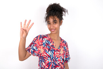Young African American woman wearing colourful dress over white wall showing and pointing up with fingers number four while smiling confident and happy.