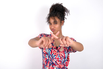 Young African American woman wearing colourful dress over white wall has rejection angry expression...
