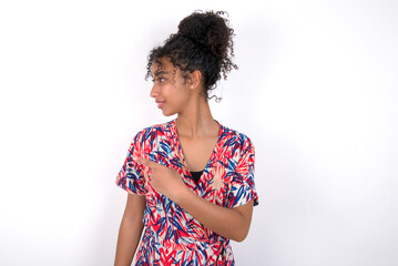 Happy cheerful smiling Young African American woman wearing colourful dress over white wall looking and pointing aside with hand. Copy space and advertisement concept.