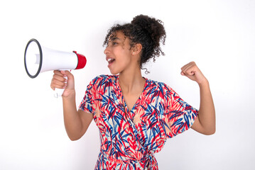 Young African American woman wearing colourful dress over white wall communicates shouting loud holding a megaphone, expressing success and positive concept, idea for marketing or sales.