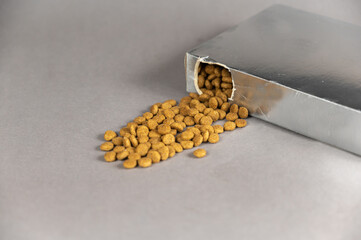 A silver rectangular box against a gray background. Pet food spilling out of the hole. Dry pelleted...