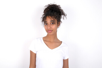 Stunned Young beautiful girl with afro hairstyle wearing white t-shirt over white wall  stares reacts on shocking news. Astonished girl holds breath