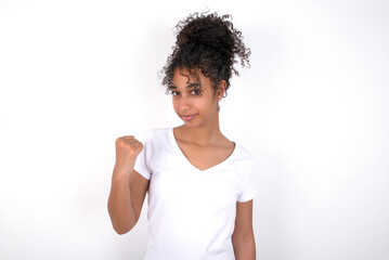 Young beautiful girl with afro hairstyle wearing white t-shirt over white shows fist has annoyed face expression going to revenge or threaten someone makes serious look. I will show you who is boss