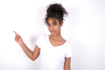 Emotive Young beautiful girl with afro hairstyle wearing white t-shirt keeps jaw dropped from shock demonstrates amazing promo points right on blank space demonstrates big shopping sale. Advertisement