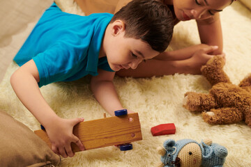 Obraz na płótnie Canvas Boy playing with various toys on furry carpet at home