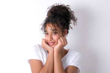 Fototapeta na wymiar Portrait of sad Young beautiful girl with afro hairstyle wearing white t-shirt over white background hands face
