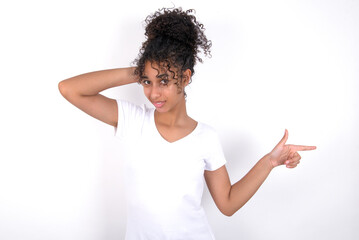 Surprised Young beautiful girl with afro hairstyle wearing white t-shirt over white background pointing at empty space holding hand on head