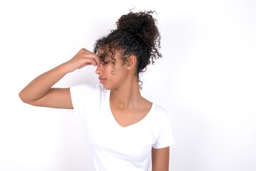 Sad Young beautiful girl with afro hairstyle wearing white t-shirt over white background suffering from headache holding hand on her face