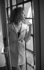 lovely sexy woman at the window .young girl in coat posing in front of camera. Fashion woman in coat. Slim young fashion model wearing white coat. portrait of young beautiful fashionable woman 