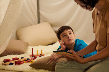 Curious little boy looking at his reading mother when they are spending weekend together