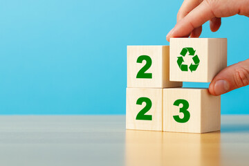 Recycling in 2023. Hand putting wooden block with recycling icon on stack of wooden blocks with...