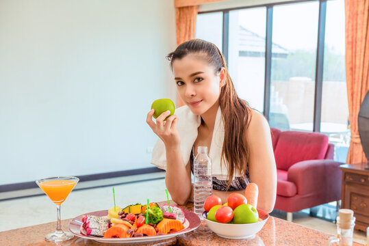 Young Asian woman with apple in her hand and fruit salad on the table.