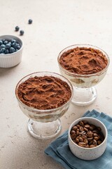 Traditional Italian dessert tiramisu with blueberries in glass. Individual trifle. Homemade layered cake with berries in cup. Selective focus.