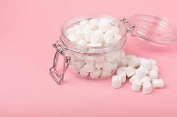 Marshmallows in a glass jar on a pink background. Chewing candy close-up. Snacks and snacks for parties. Spice for coffee and cocoa. Winter food concept. Space for text. Place to copy.