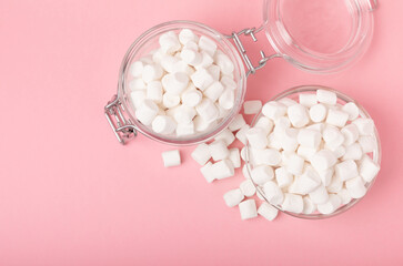 Marshmallows in a glass bowl and a jar on a pink background.Sweets and snacks for a snack.Chewy candy close-up.Copy space.Place for text.