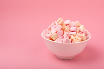 Fototapeta na wymiar Marshmallows in a ceramic bowl on a pink background. Chewing candy with strawberry flavor close-up. Snacks and snacks for parties. Spice for coffee and cocoa. Winter food concept. Space for text. 