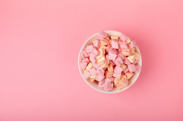 Marshmallows in a ceramic bowl on a pink background. Chewing candy with strawberry flavor close-up. Snacks and snacks for parties. Spice for coffee and cocoa. Winter food concept. Space for text. 