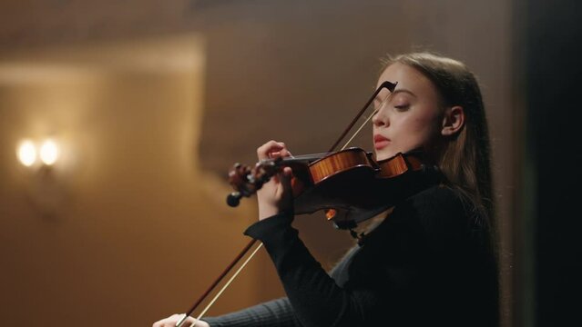 inspired and talented woman fiddler in symphonic orchestra on scene of music hall