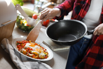 Woman putting freshly fried eggs with vegetables onto plate in kitchen, closeup