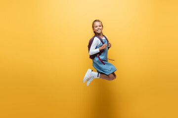 Fototapeta Cheerful schoolgirl with backpack jumping on yellow background. obraz