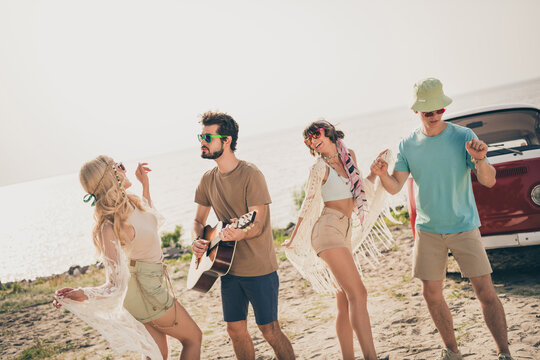 Photo of four inspired buddies spend free time guy play guitar live music wear casual outfit nature seaside beach outside
