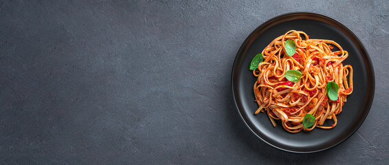 Pasta with tomato sauce and fresh basil on a dark background. View from above. Vegetarian food.