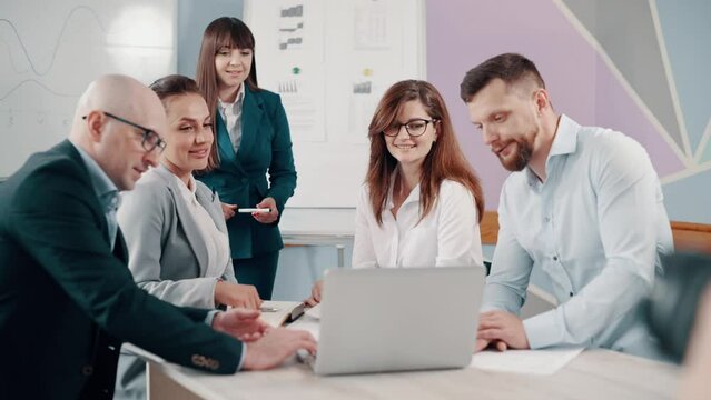 A team of business people are discussing the project together in the office. The team sits at a table and looks at a laptop screen.