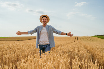 Happy farmer with arms outstretched standing in his growing wheat field.	